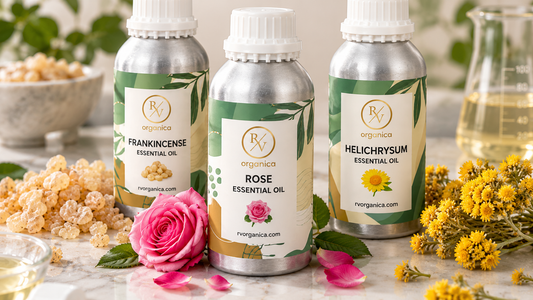 RV Organica frankincense, rose and helichrysum essential oil bottles in silver aluminium packaging with frankincense resin, a pink rose and yellow helichrysum flowers on a marble lab counter