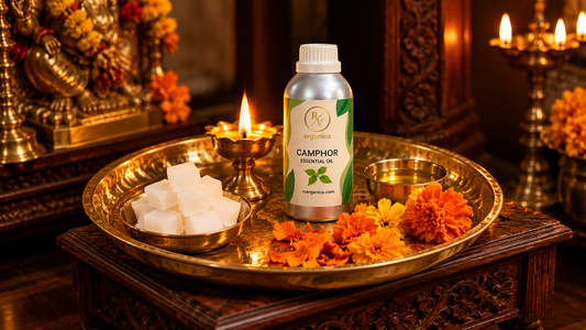 RV Organica Camphor Essential Oil bottle on a brass aarti thali with camphor tablets, a lit diya, a katori of kapur oil and marigolds