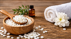 White emulsifying wax pellets in wooden bowl with essential oil bottle and white flower