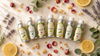 RV Organica essential oils collection — Lemongrass, Eucalyptus, Citronella and Geranium essential oils in aluminium bottles arranged on marble with rose petals, lemon slices and lavender sprigs