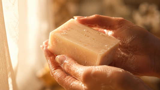 Hands holding a creamy white handmade soap bar with rich lather,  made using shea butter melt and pour soap base, in warm golden  morning light