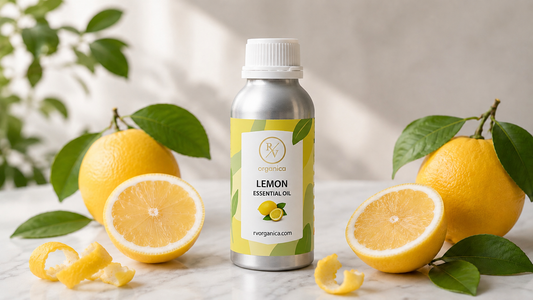 RV Organica Lemon Essential Oil silver aluminium bottle surrounded by fresh lemon halves, lemon peels and green leaves on white marble — pure cold pressed citrus essential oil by rvorganica.com