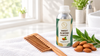 RV Organica sweet almond carrier oil bottle with wooden comb, almonds, and fresh green leaves on a white towel in a bright bathroom setting