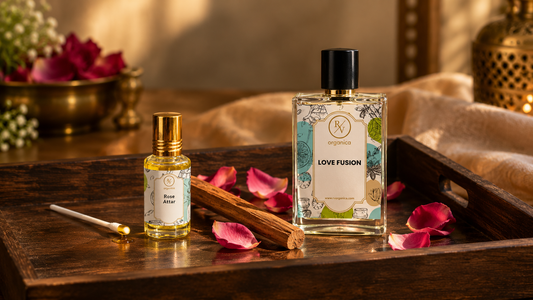 Premium RV Organica Rose Attar and Love Fusion perfume bottles arranged on a dark wooden tray with rose petals and sandalwood in warm luxury lighting.