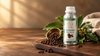 RV Organica clove bud essential oil bottle with dried cloves, fresh green leaves, and a brass bowl on a rustic wooden surface.