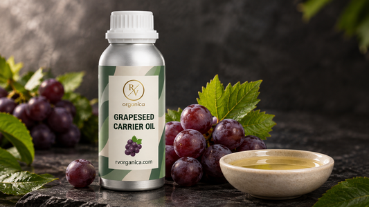 RV Organica grapeseed carrier oil bottle beside red grapes and a stone dish of light golden oil on dark slate