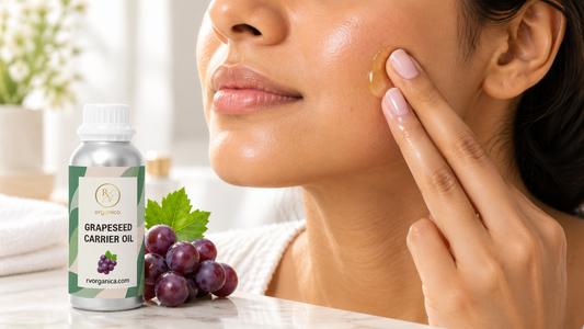 Woman pressing a drop of grapeseed oil into her cheek beside an RV Organica grapeseed carrier oil bottle and red grapes on a marble vanity