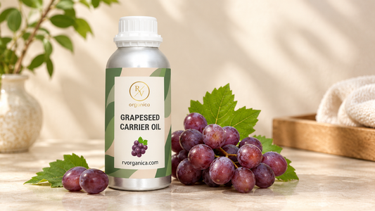 RV Organica grapeseed carrier oil bottle with fresh red grapes and vine leaves on a sunlit stone counter beside a vase and folded towel
