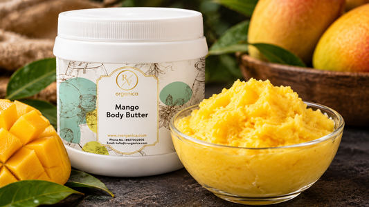 RV Organica Mango Body Butter jar beside a glass bowl of golden whipped mango butter, a cut fresh mango and mango leaves on dark stone