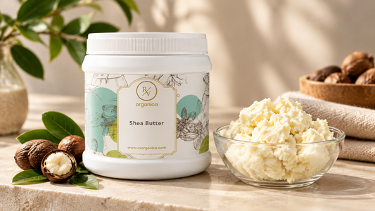 RV Organica Shea Butter jar beside a glass bowl of raw shea butter, whole shea nuts and green leaves on a beige stone counter