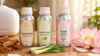 RV Organica Sandalwood, Lemongrass and Divine Lotus fragrance oil bottles beside a white ultrasonic diffuser, with sandalwood sticks, fresh lemongrass and a pink lotus on a wooden table