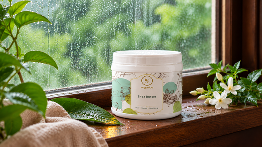 RV Organica Shea Butter jar on a wet wooden windowsill with raindrops on the glass, green foliage outside, jasmine flowers and a towel