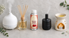 RV Organica Royal Rose fragrance oil bottle placed between a white ultrasonic diffuser, a glass reed diffuser, a black nebulizing diffuser and a ceramic tealight oil burner on a grey stone surface