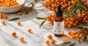 "RV Organica Sea Buckthorn Facial Oil – 30ml amber glass dropper bottle on a white marble surface, surrounded by fresh orange sea buckthorn berries and green leaves. Label reads: 'Radiant Skin, Naturally'."