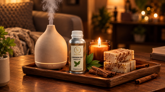 Ceramic diffuser releasing mist beside a cinnamon leaf essential oil bottle, a lit amber jar candle and handmade cinnamon soap bars on a wooden tray in a cosy living room