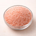 Himalayan pink salt crystals in a glass bowl, top view on neutral background